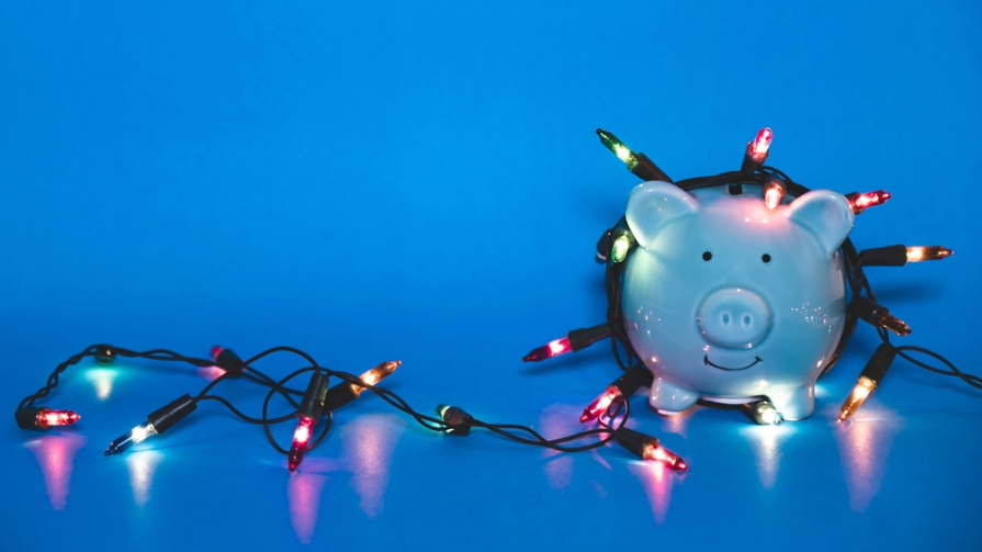 Holiday lights partly wrapped around a smiling piggy bank.
